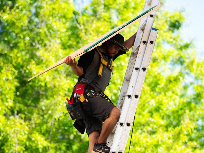 roofing-contractor-carrying-materials-up-ladder-jobsite roofing-contractor-carrying-materials-up-ladder-jobsite